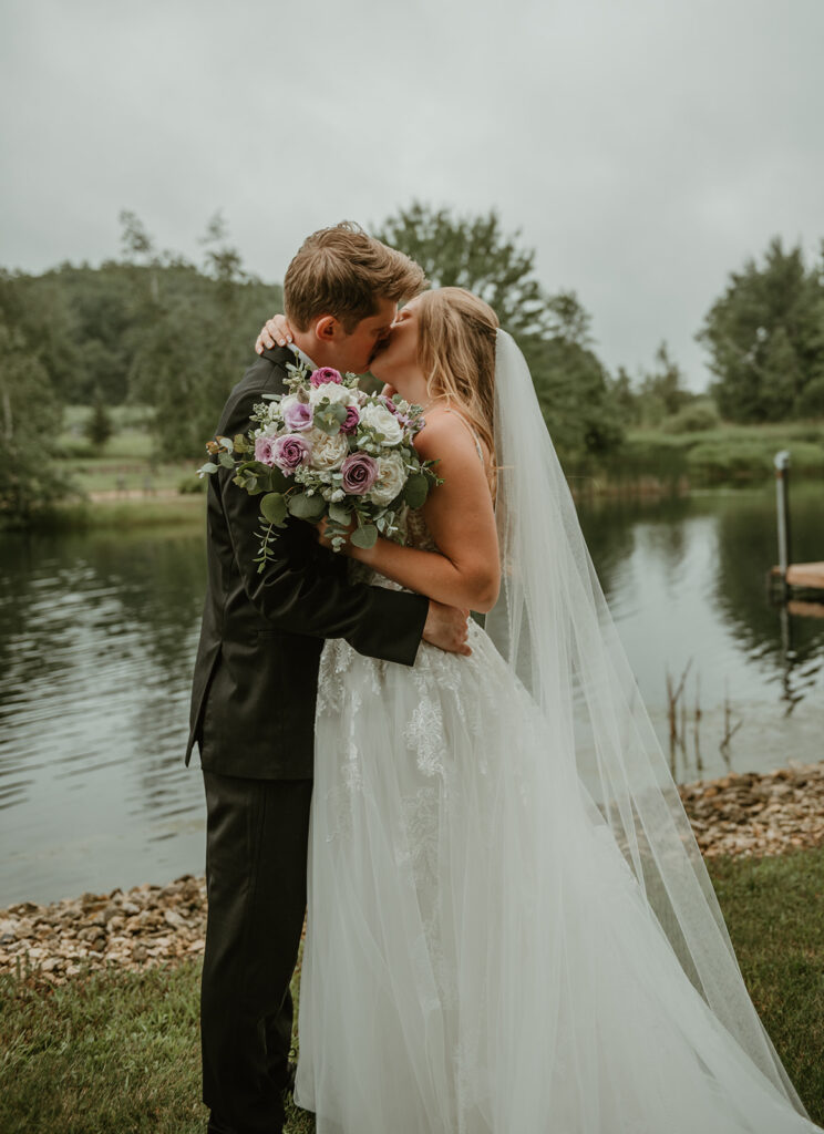 a bride and groom kissing on the edge of a pond