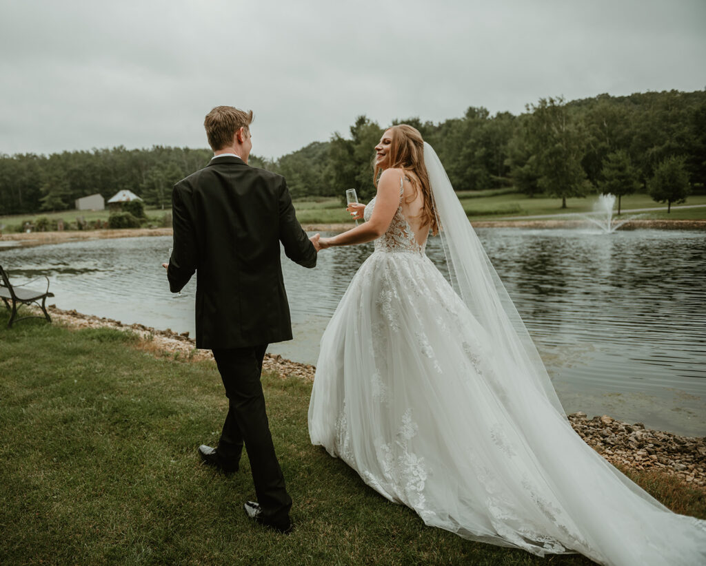 A bride and groom holding hands walking along the pond at dixons apple orchard in cadott wi