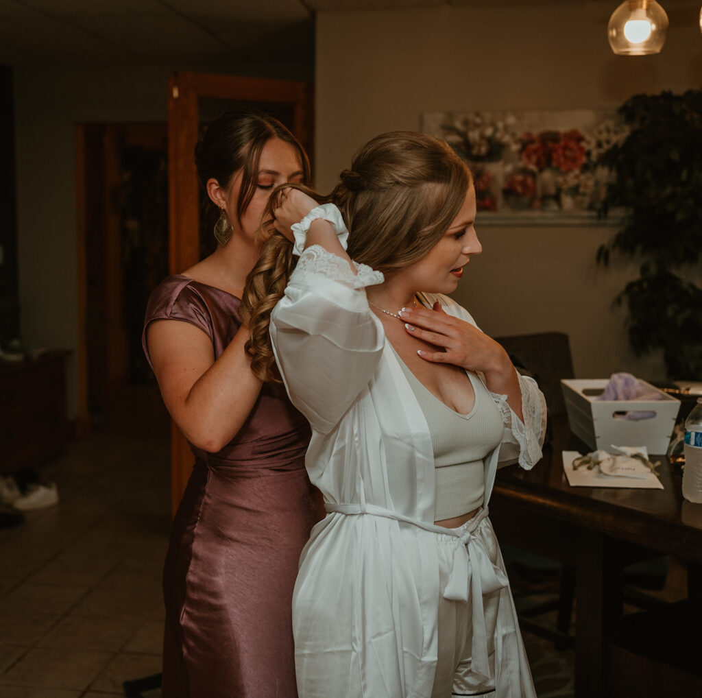 the brides assistant helping her put on her wedding necklace