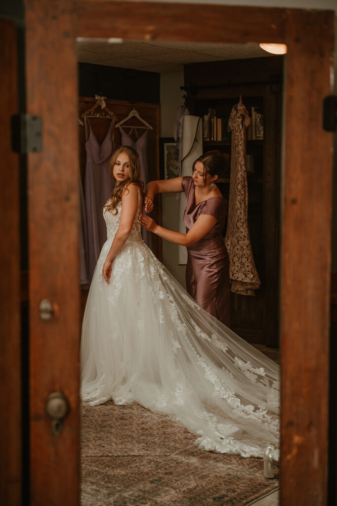 the bride's assistant helping her button up her dress