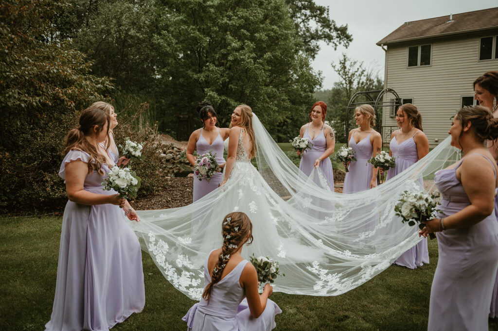 a bride smiling with her bridesmaids surrounding her fixing her up and making sure she looks perfect before her wedding ceremony