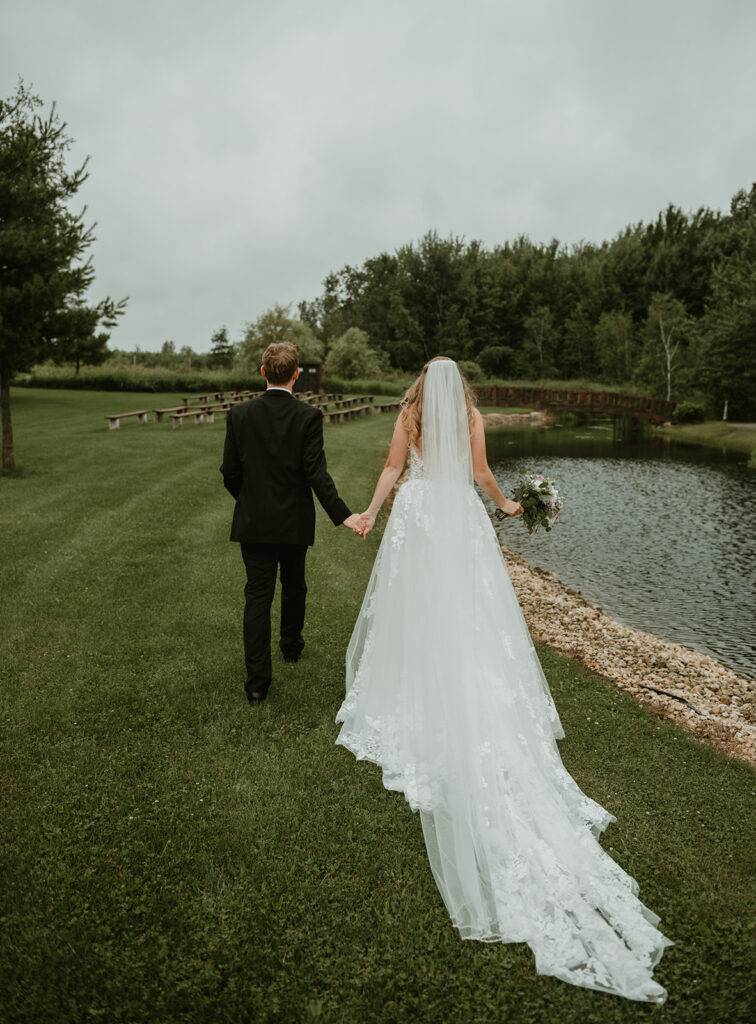 a bride and groom holding hands walking along the pond at dixons apple orchard in cadott wisconsin