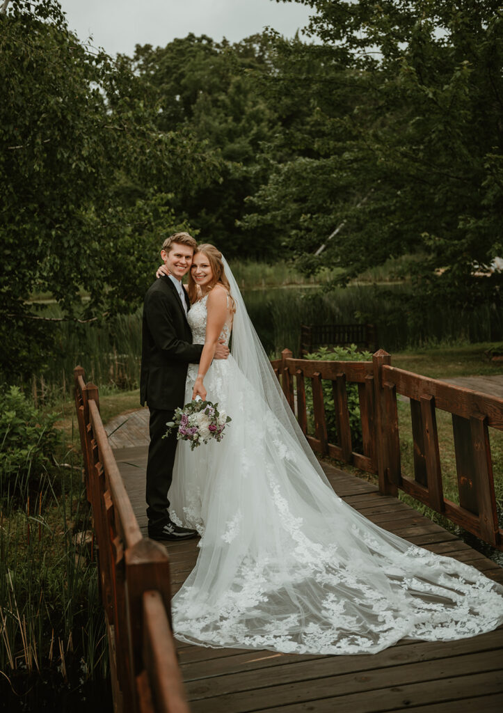 a bride and groom standing together on a bridge over the pond at dixons apple orchard