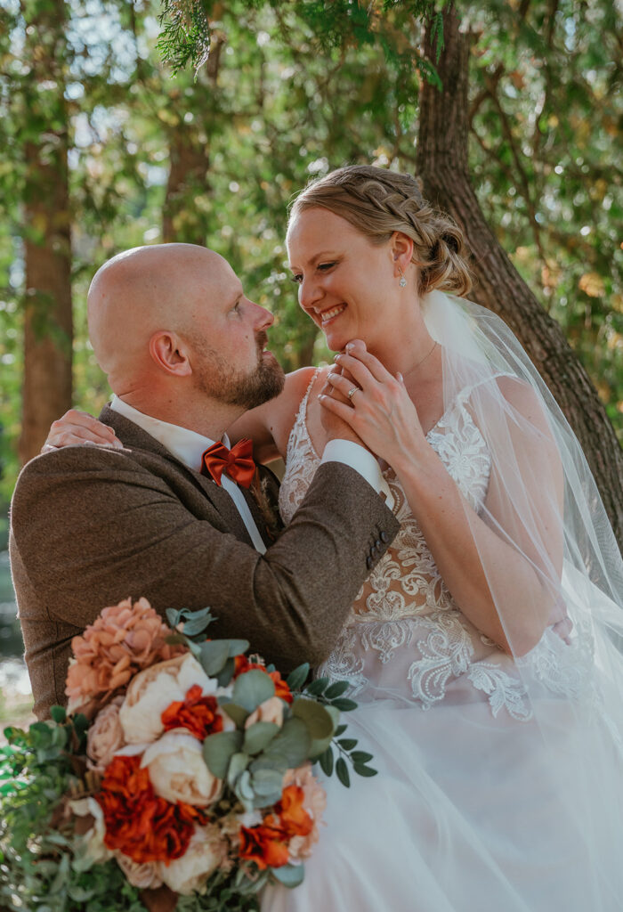 a bride sitting in a tree and the groom standing next to her in the woods