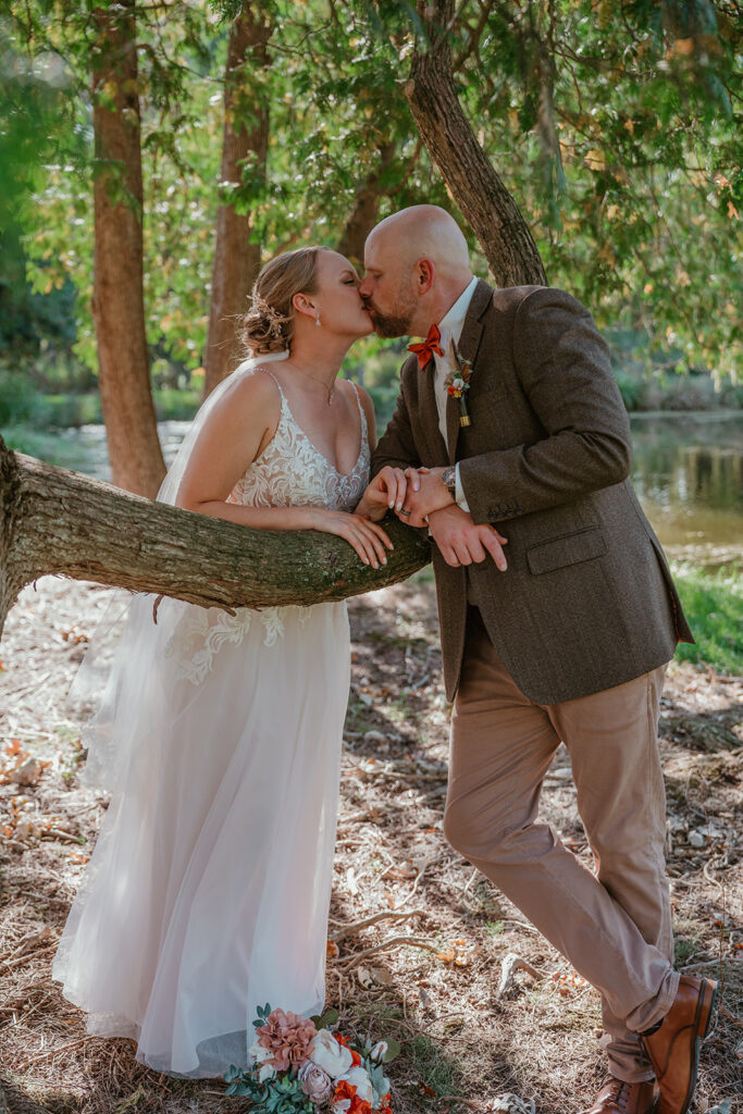 a bride and groom standing on opposites sides of a fallen tree kissing each other on their wedding day