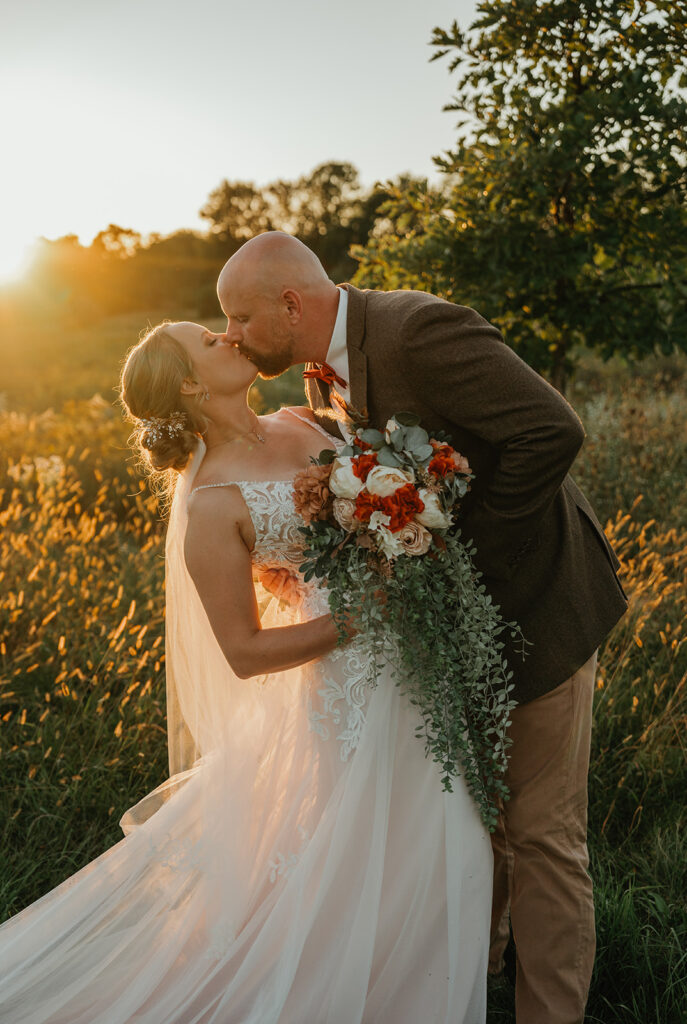 a bride and groom kissing in a field 
 at homestead meadows farm during sunset on their wedding day