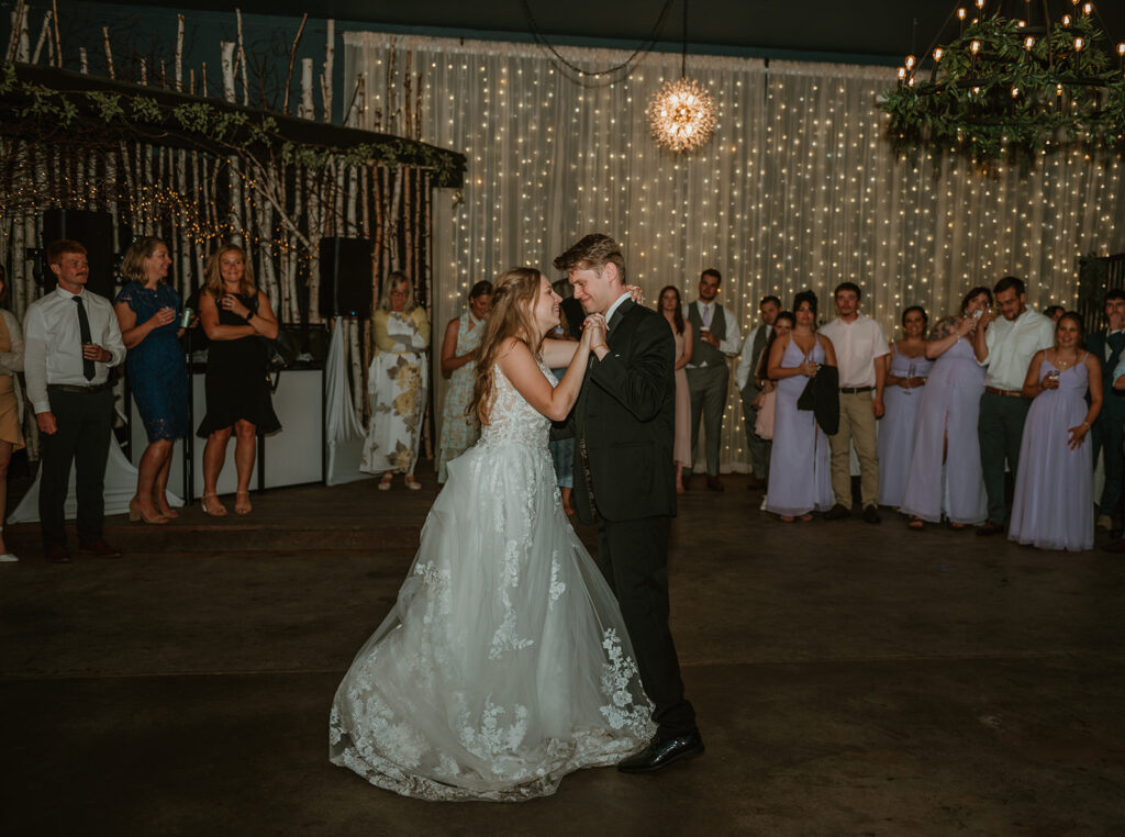 bride and groom having their first dance with their family surrounding them in the reception space at dixons apple orchard