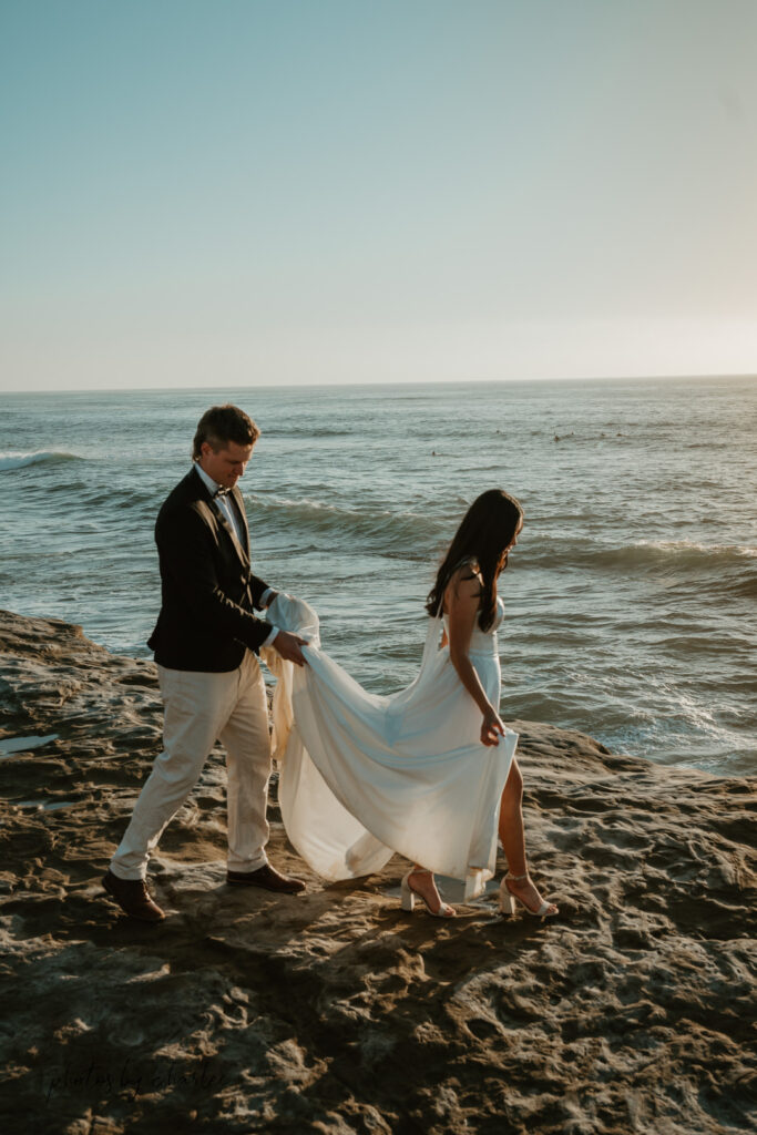 Groom assists bride across the rocky landscape at Sunset Cliffs, intimate elopement moment, San Diego photographer