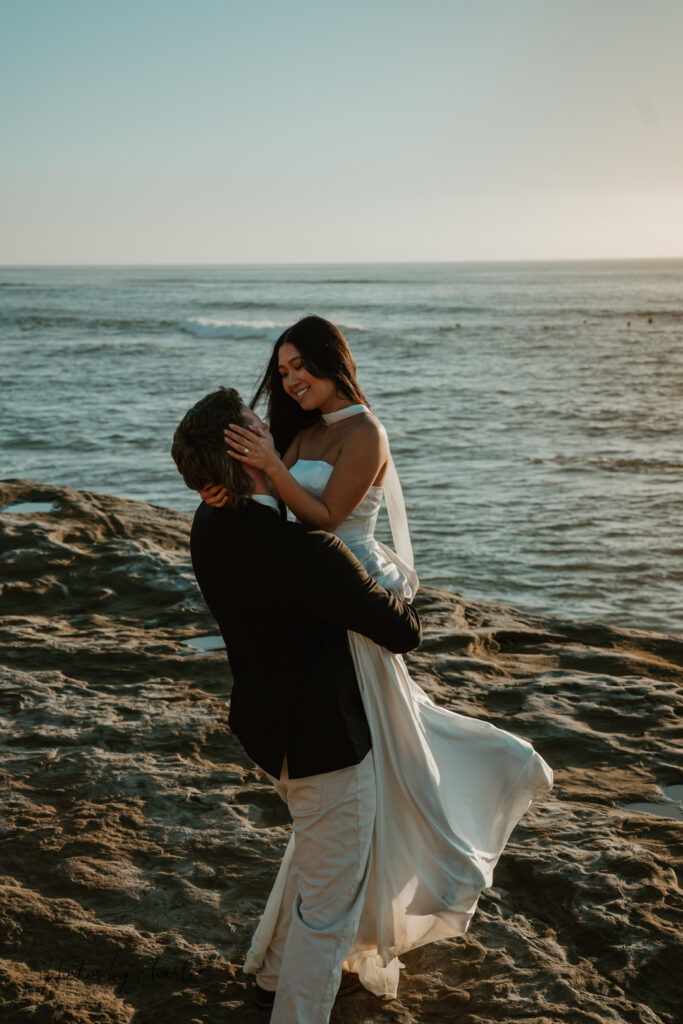 Groom playfully spins his bride near the dramatic cliff edge at Sunset Cliffs, enjoying the breathtaking ocean view from a safe viewpoint during their San Diego elopement